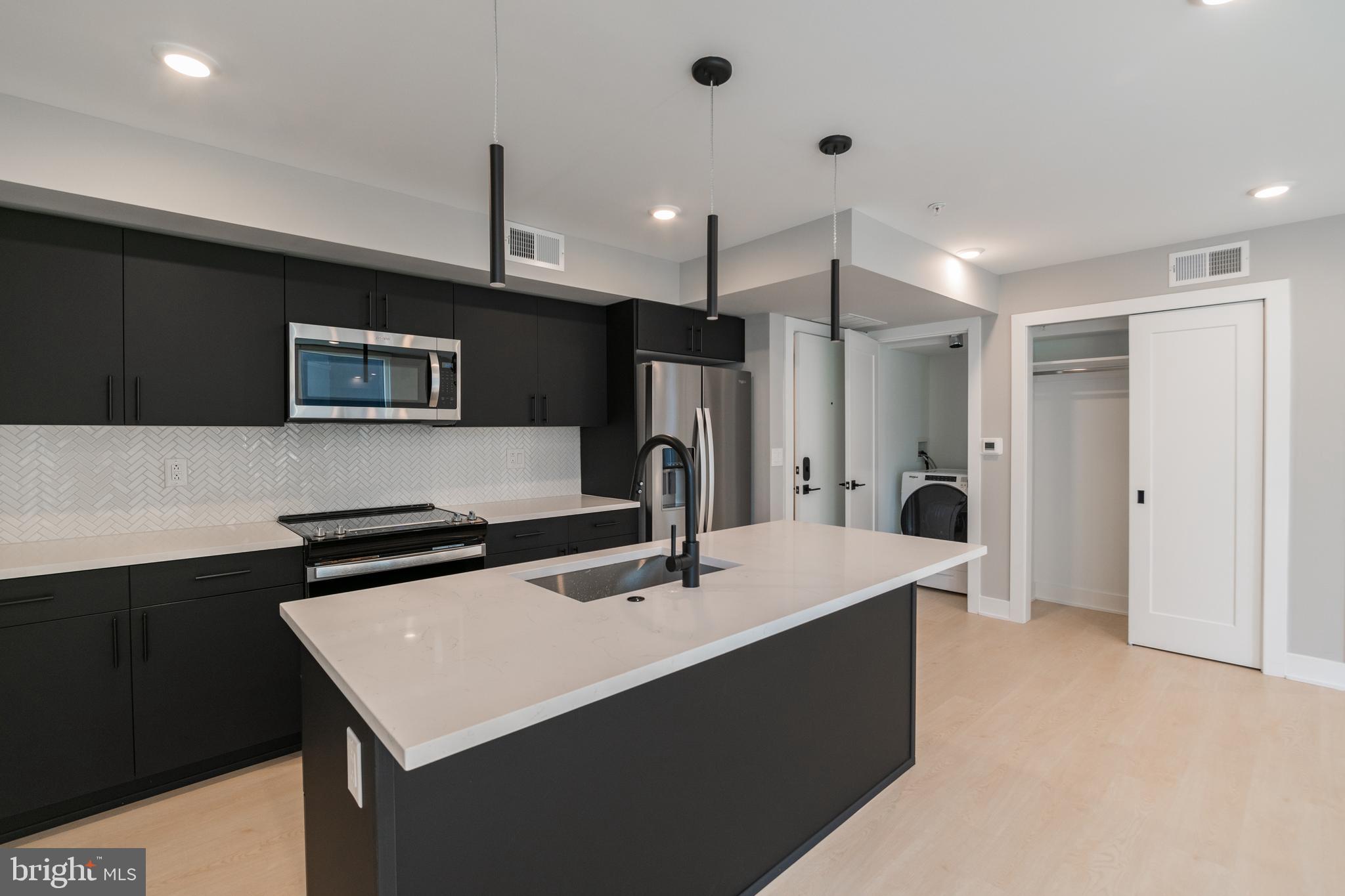 6604 Ridge Avenue, Unit 401 Philadelphia, PA 19128 - Photo 2 of 11 a kitchen with a sink a refrigerator a microwave a island and cabinets
