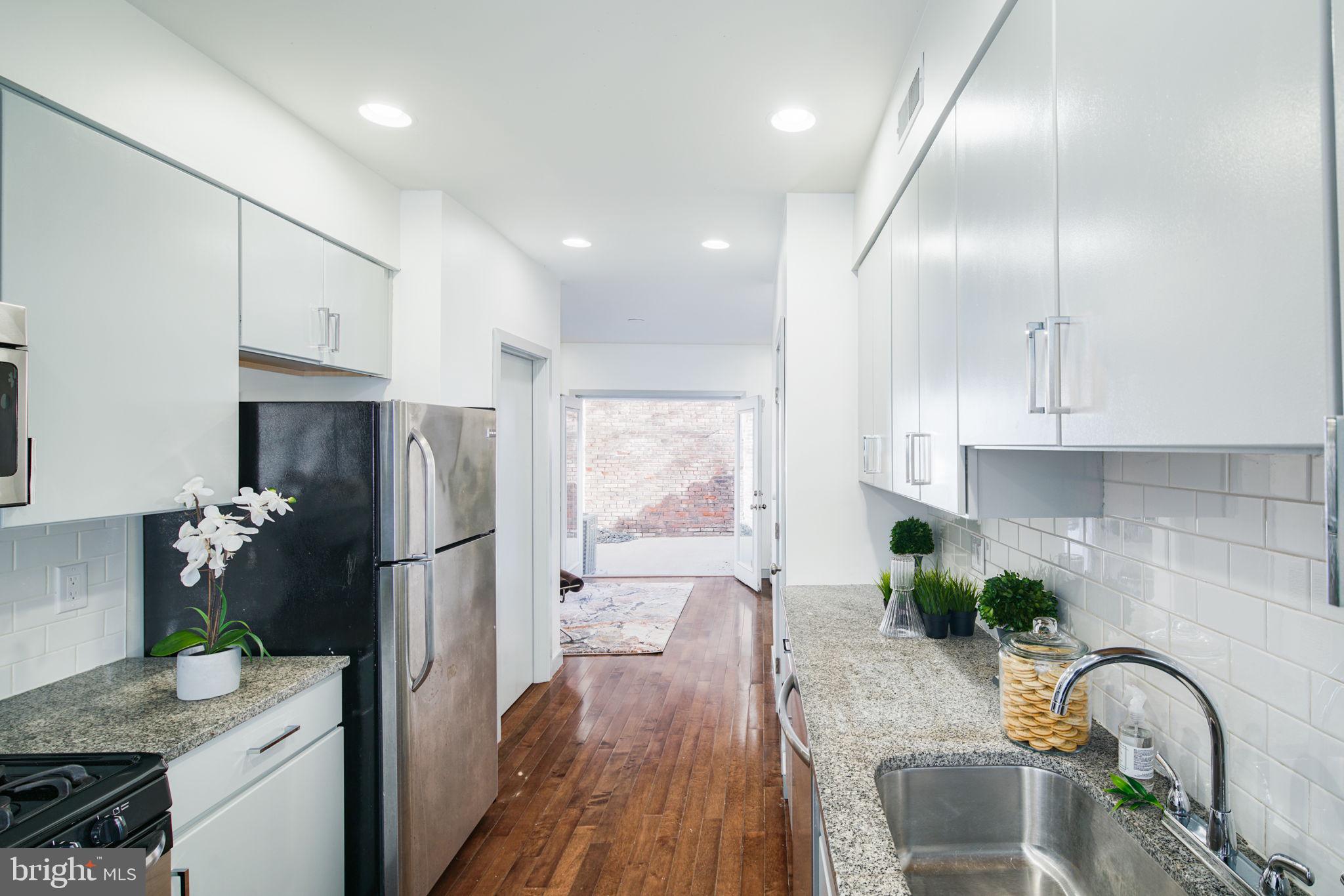 1235 North Taney Street Philadelphia, PA 19121 - Photo 7 of 28 a kitchen with granite countertop stainless steel appliances a refrigerator a sink a stove and white cabinets with wooden floor