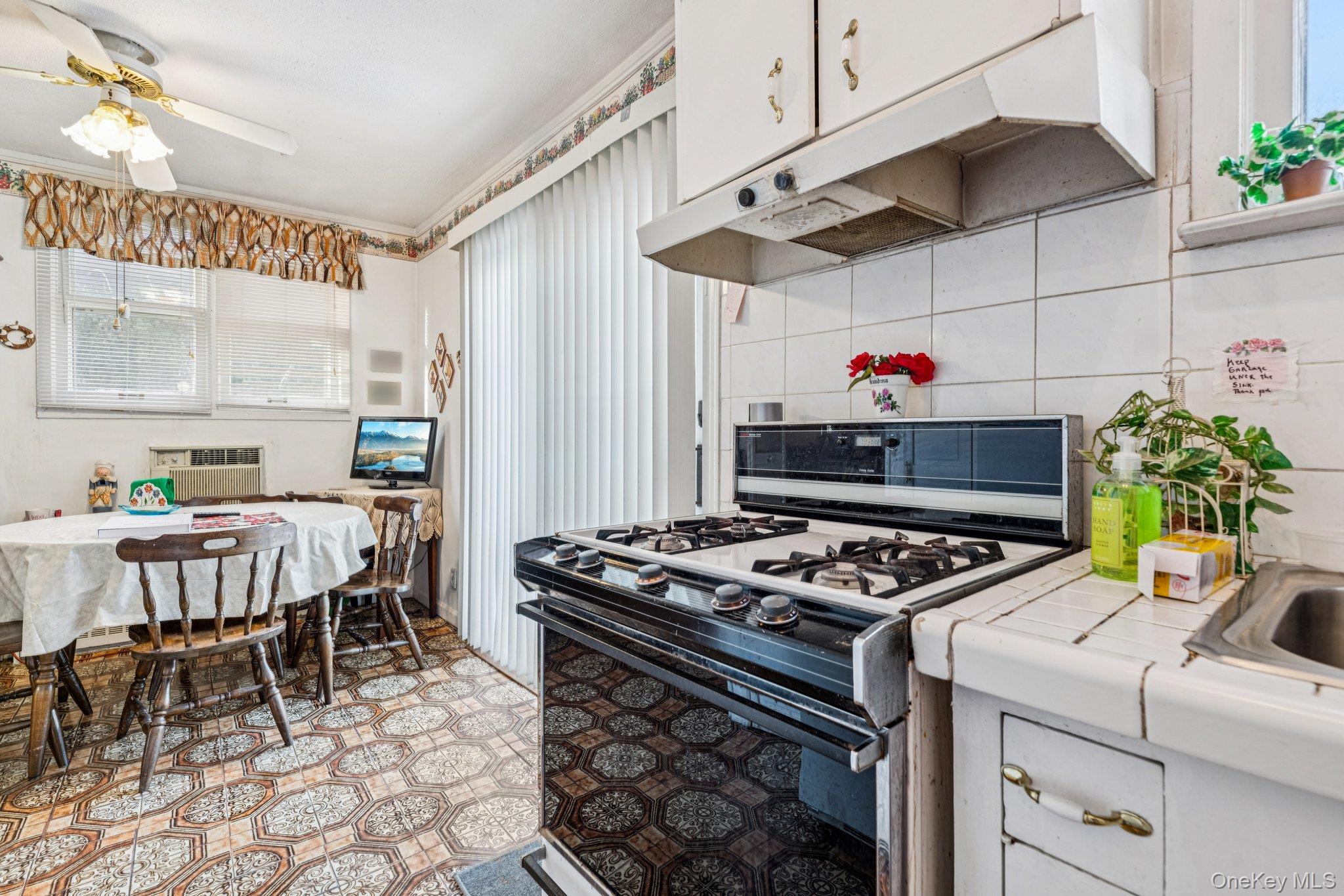 189 Surrey Commons Lynbrook, NY 11563 - Photo 12 of 14 Kitchen featuring gas range oven, under cabinet range hood, tile countertops, and white cabinetry