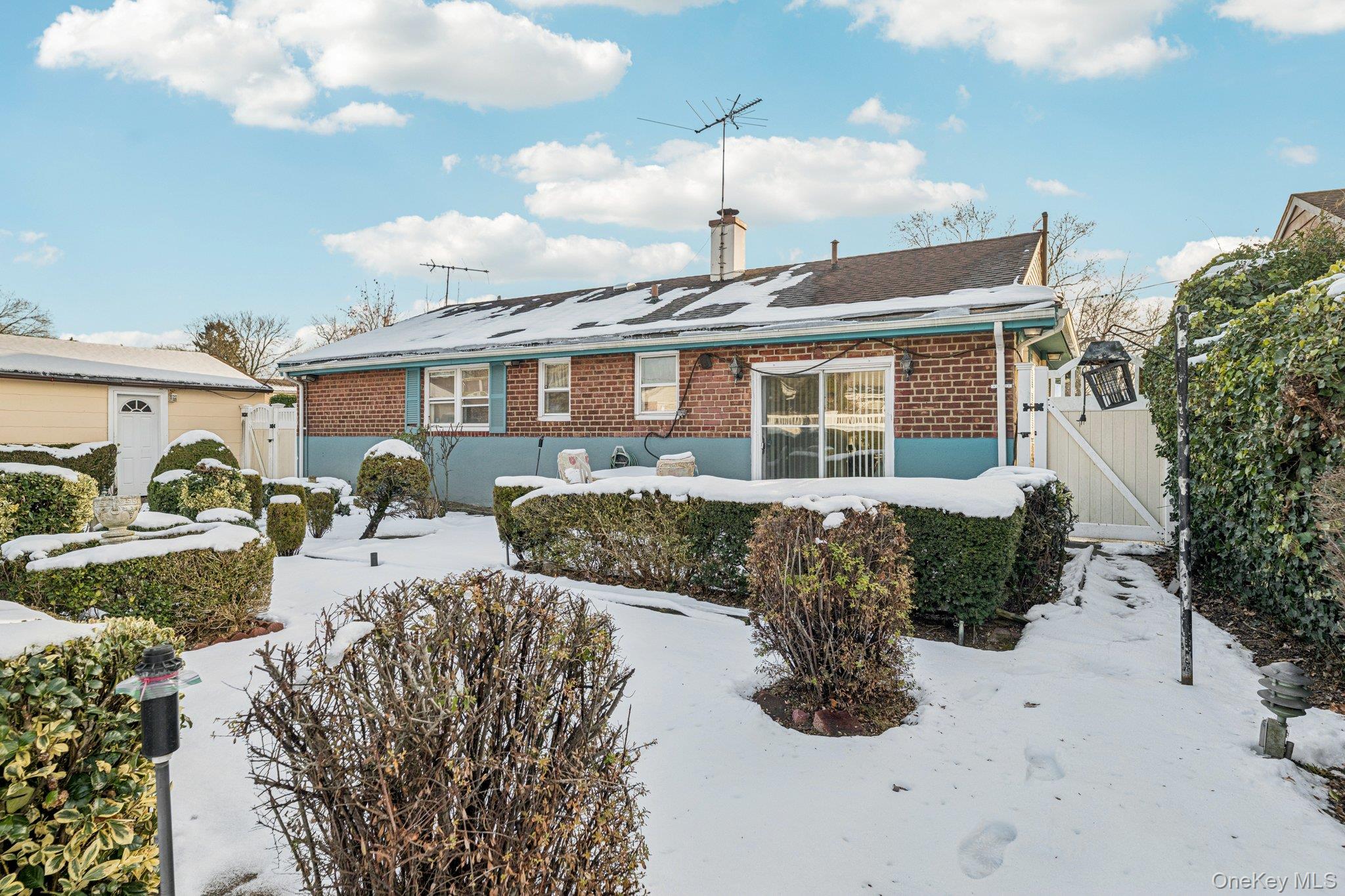 189 Surrey Commons Lynbrook, NY 11563 - Photo 4 of 14 Ranch-style home featuring a gate, brick siding, a chimney, and roof mounted solar panels