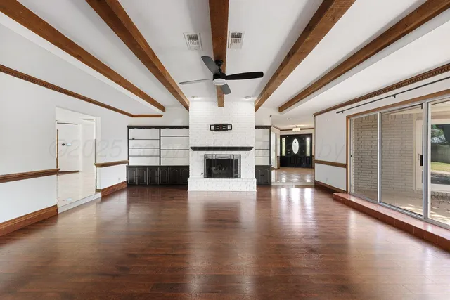 a view of an empty room with wooden floor fireplace and a window