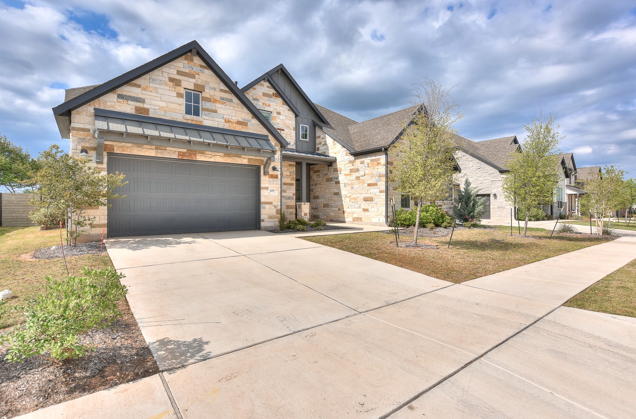 309 Wolf Rdg Road Georgetown, TX 78628 - Photo 2 of 39 View of front of home featuring driveway, stone siding, a garage, a front yard, and a standing seam roof