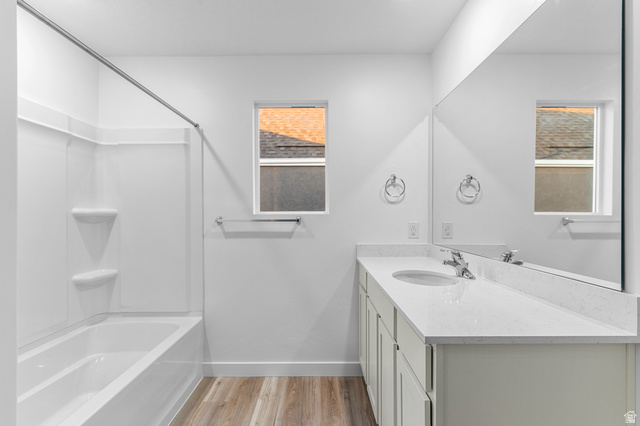 2829 North 710 West, Unit 15 Logan, UT 84321 - Photo 18 of 23 Bathroom featuring a white integrated tub and shower unit, a spacious vanity with a white countertop and undermount sink, a large wall-mounted mirror, and wood-finish flooring