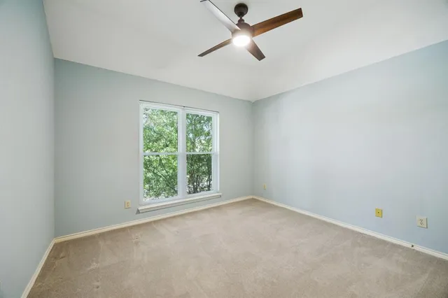 an empty room with chandelier fan and windows