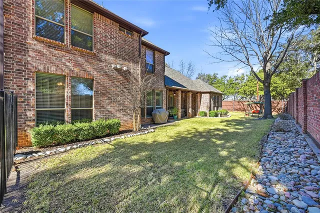 a brick house with a big yard plants and large tree