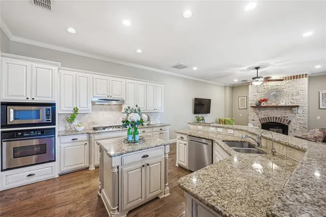 a kitchen with stainless steel appliances granite countertop a stove top oven a sink dishwasher and a refrigerator with wooden floor