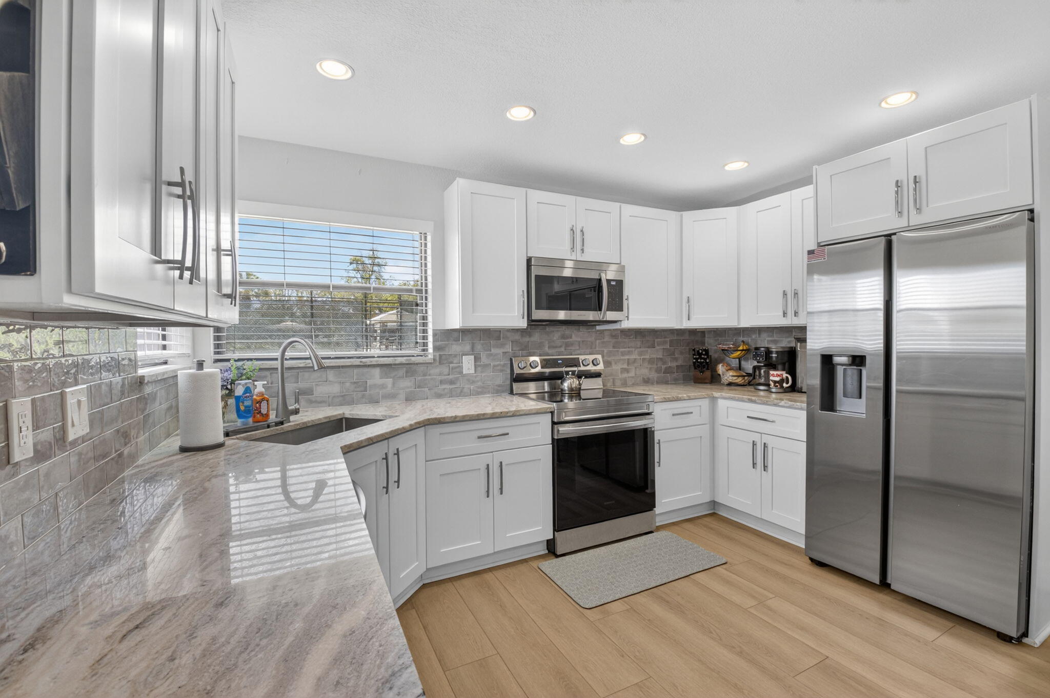 a kitchen with stainless steel appliances granite countertop a stove a sink dishwasher a refrigerator and a microwave oven with wooden floor