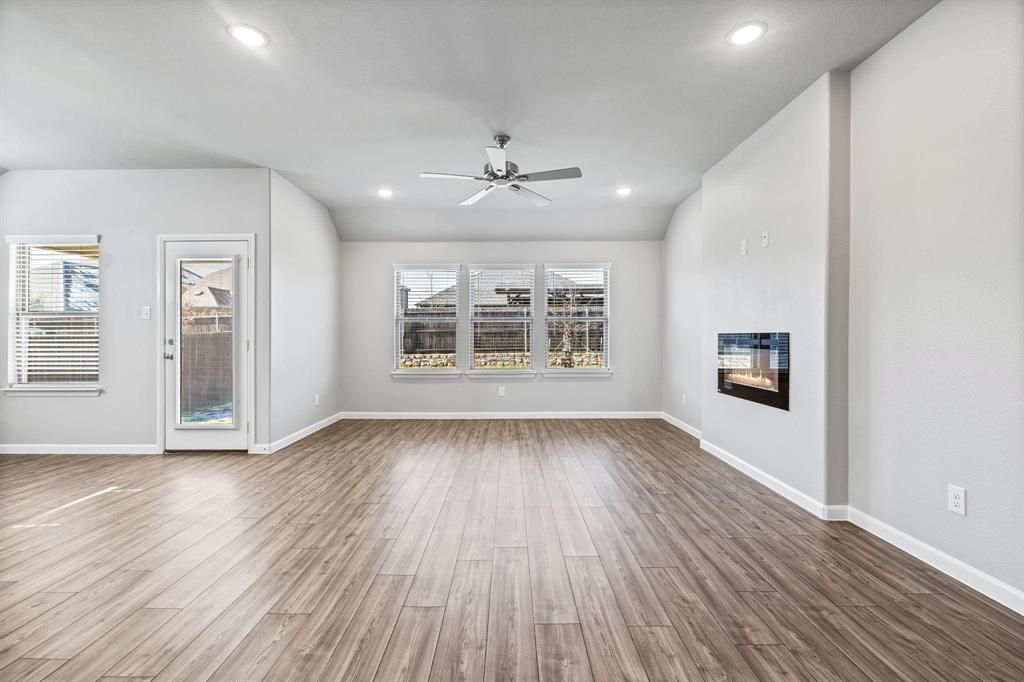 620 Shade Tree Way Princeton, TX 75407 - Photo 12 of 35 an empty room with wooden floor chandelier fan and windows