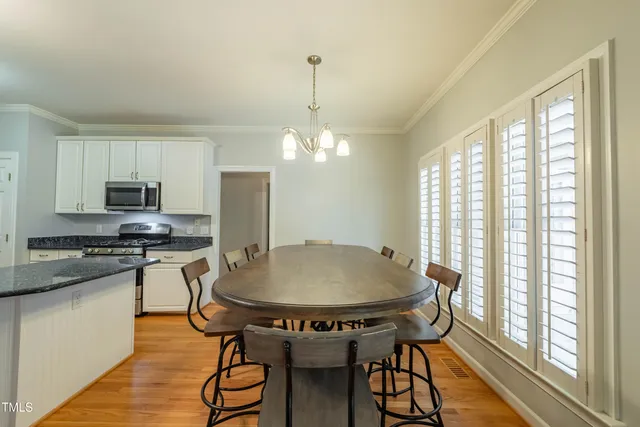 a kitchen with stainless steel appliances granite countertop a stove a refrigerator a sink a dining table and chairs with wooden floor