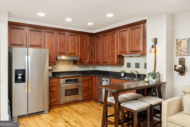 a kitchen with stainless steel appliances granite countertop a stove a refrigerator a sink a dining table and chairs with wooden floor