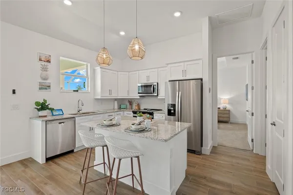 a kitchen with stainless steel appliances granite countertop a refrigerator a sink dishwasher a stove and white cabinets with wooden floor