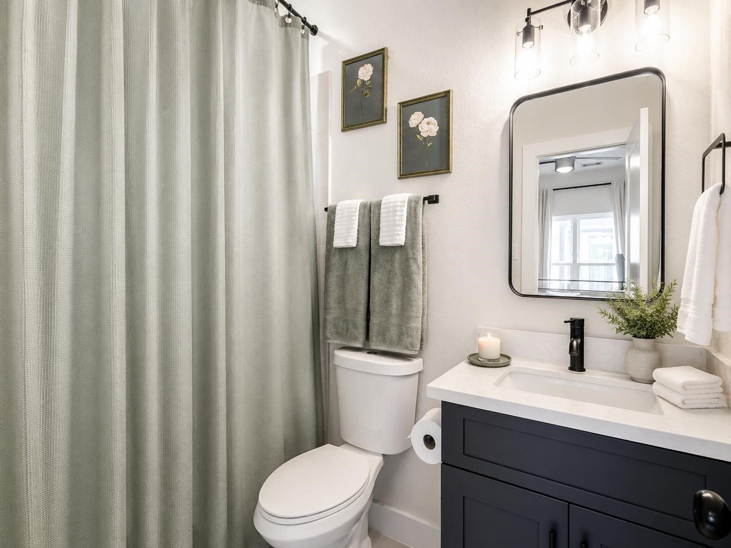 5407 Lee Street Houston, TX 77020 - Photo 11 of 17 This bathroom features a modern design with a sleek vanity, a large mirror, and elegant lighting. It has a shower with a green curtain and decorative wall art, creating a fresh and inviting atmosphere.