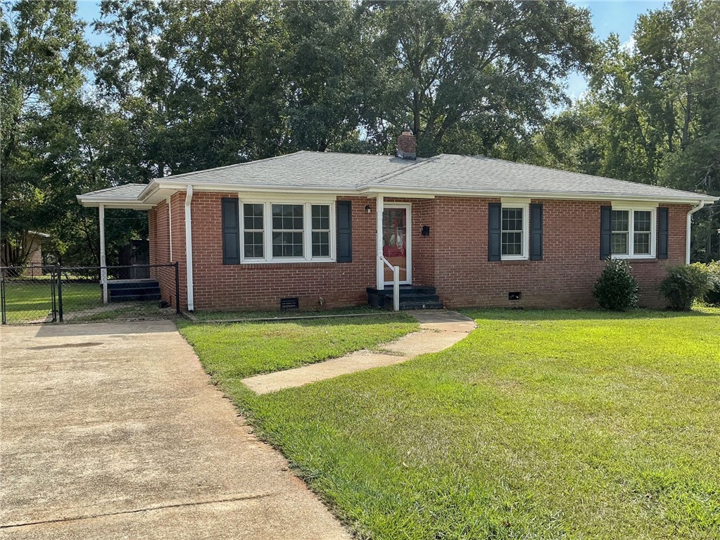 A classic brick exterior features dark shutters, a concrete driveway, and a grassy front lawn.