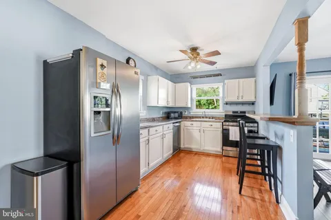 a kitchen with granite countertop a refrigerator a sink dishwasher a stove and white cabinets with wooden floor