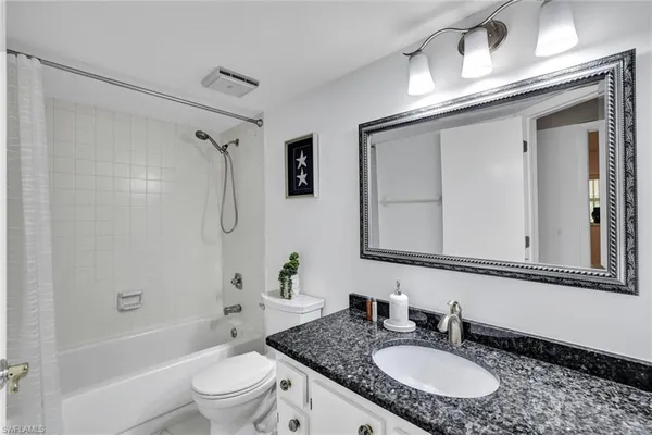 a bathroom with a granite countertop sink a toilet a mirror a bathtub and shower