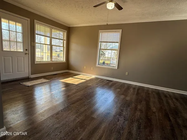 an empty room with wooden floor chandelier fan and windows