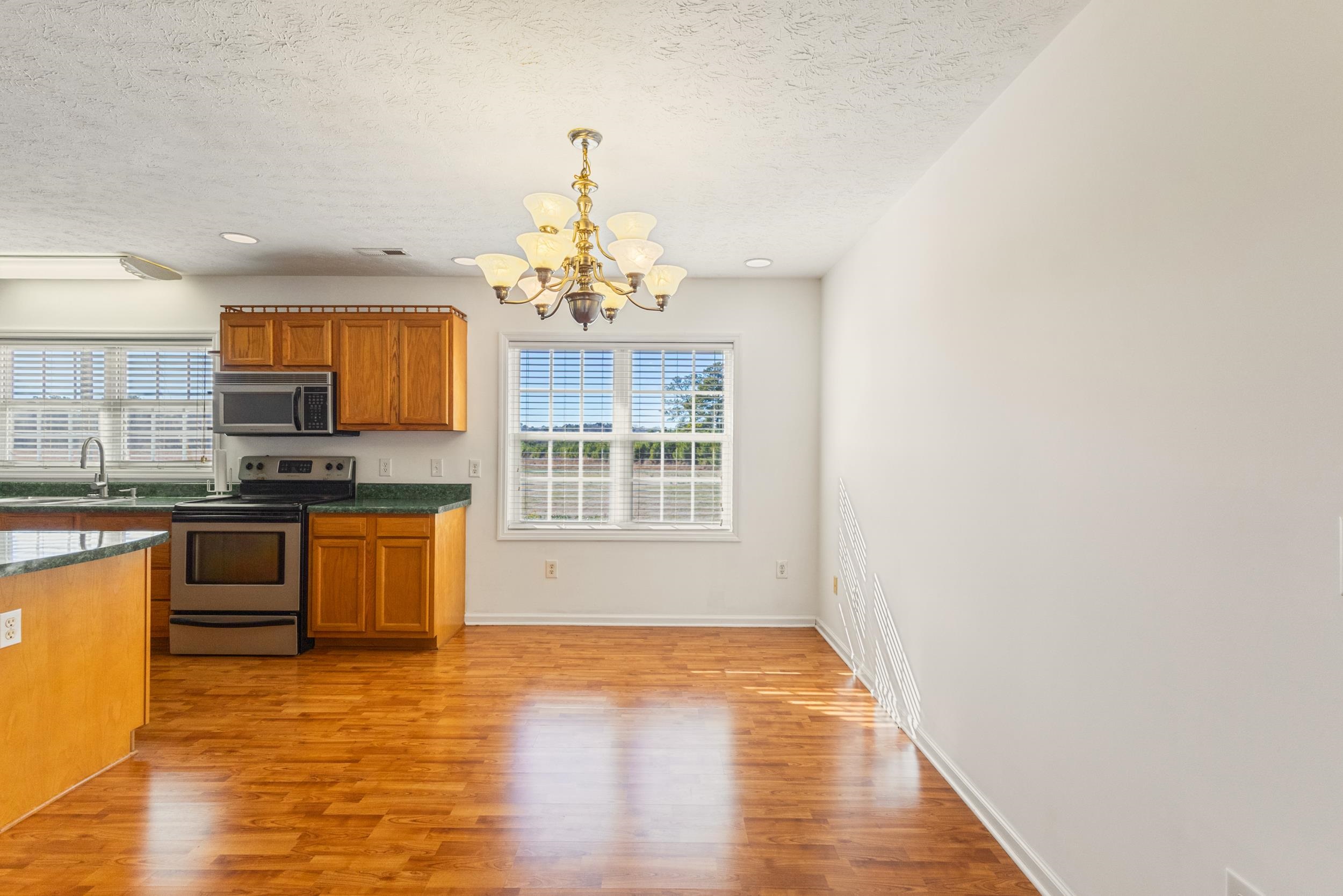 3923 State Rd S-26-33 Green Sea, SC 29545 - Photo 23 of 40 Kitchen featuring a chandelier, stainless steel appliances, brown cabinetry, light wood finished floors, and a textured ceiling