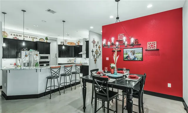 a kitchen with stainless steel appliances kitchen island granite countertop a dining table chairs and a refrigerator