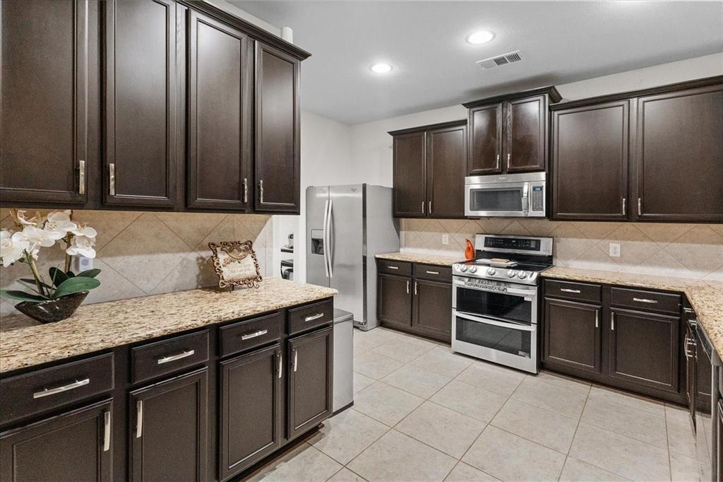 2529 Spring Meadows Drive Denton, TX 76209 - Photo 6 of 29 a kitchen with stainless steel appliances granite countertop a stove a sink and a microwave