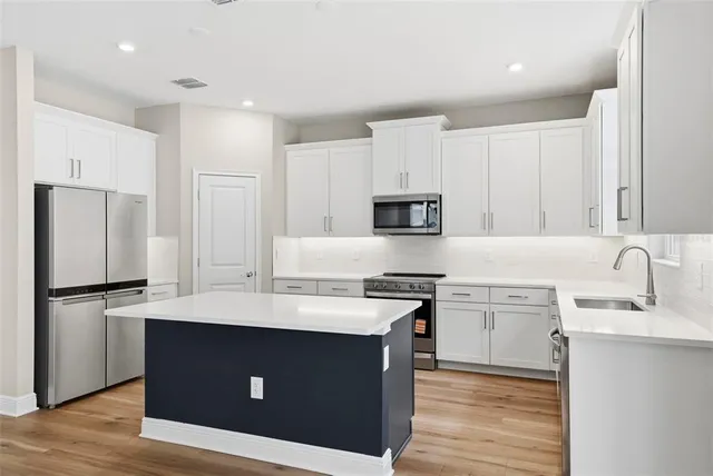 a kitchen with a sink white stove refrigerator and white cabinets with wooden floor