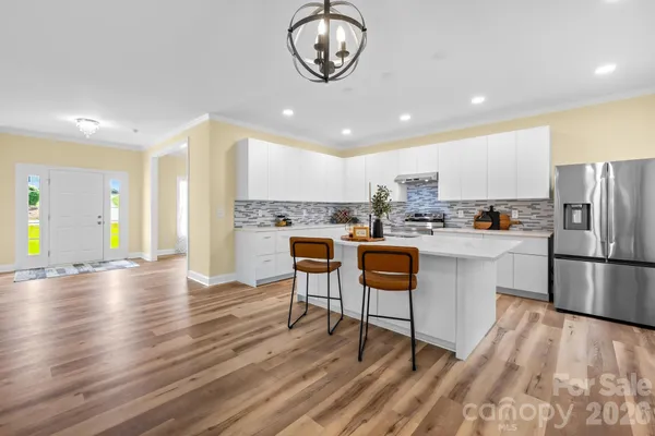 a kitchen with stainless steel appliances granite countertop a refrigerator a stove top oven a sink dishwasher and white cabinets with wooden floor