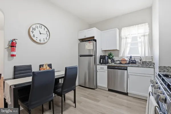 a kitchen with stainless steel appliances granite countertop a dining table chairs cabinets a large window and a refrigerator
