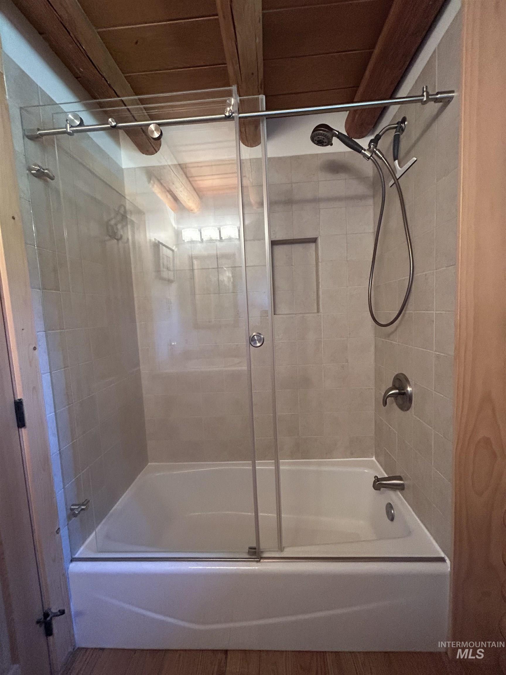 35 Sawtooth Way Stanley, ID 83278 - Photo 23 of 36 Bathtub with clear glass sliding shower doors and brushed metal hardware, featuring a tiled surround with a recessed niche and a handheld shower fixture