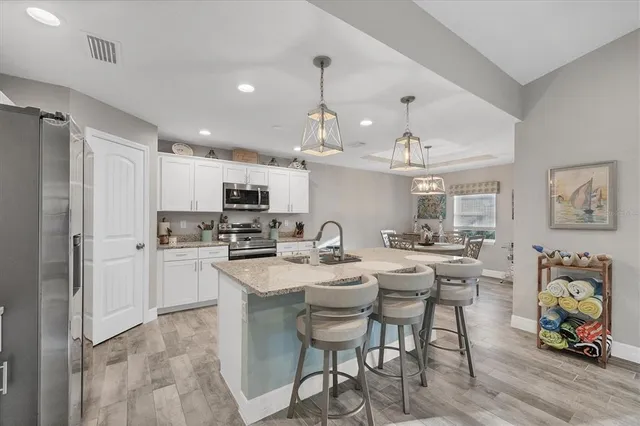 a kitchen with stainless steel appliances kitchen island granite countertop a dining table chairs refrigerator and cabinets