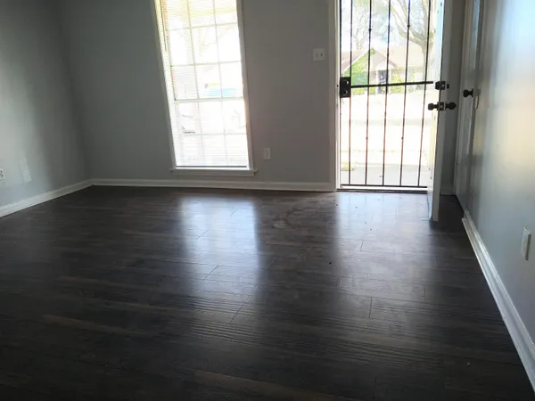 an empty room with wooden floor and windows with curtains