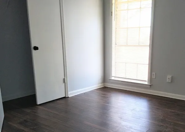 an empty room with wooden floor and windows with curtains