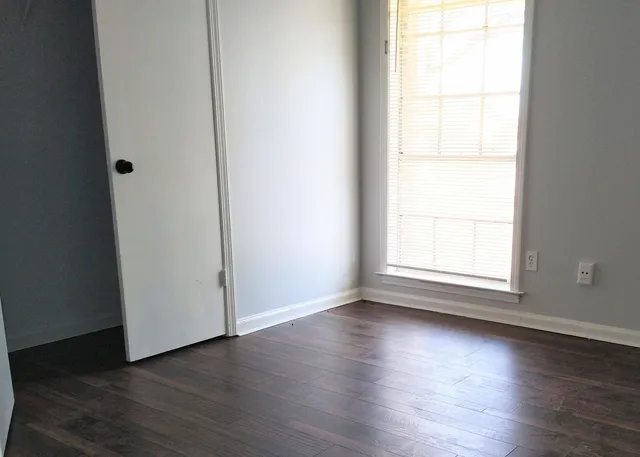 an empty room with wooden floor and windows with curtains