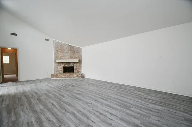 a view of an empty room with wooden floor fireplace and a window