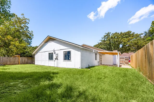 a white house with a small yard and big trees with wooden fence