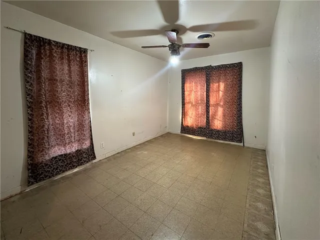 an empty room with a chandelier fan and windows