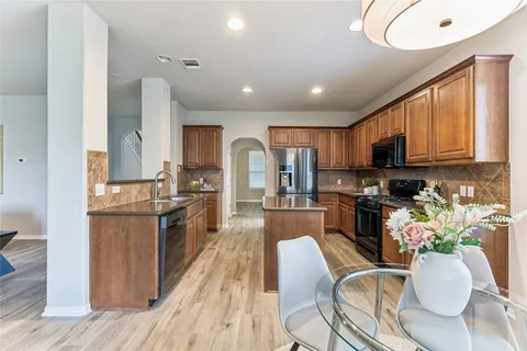 a kitchen with stainless steel appliances granite countertop wooden cabinets a sink dishwasher a stove and a refrigerator with wooden floor