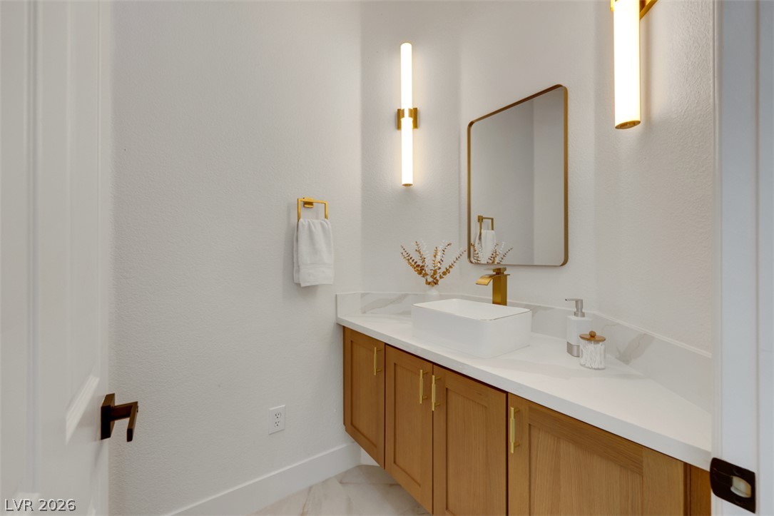 5015 Rivedro Street Las Vegas, NV 89135 - Photo 19 of 91 A well-lit powder room showcases a floating wood vanity with a vessel sink and sleek gold fixtures.