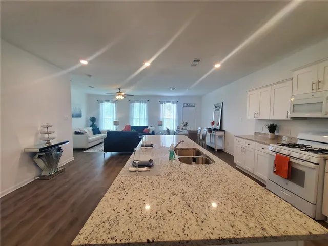 a large white kitchen with stainless steel appliances granite countertop a stove a sink a dining table and chairs with wooden floor