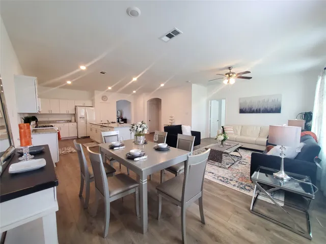 a dining room with wooden floor a chandelier fan a wooden table and chairs