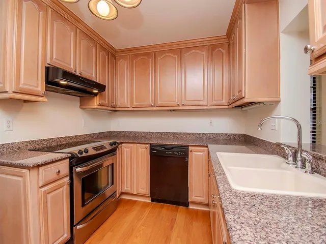 a kitchen with granite countertop a stove a sink and dishwasher wooden cabinets with granite countertops