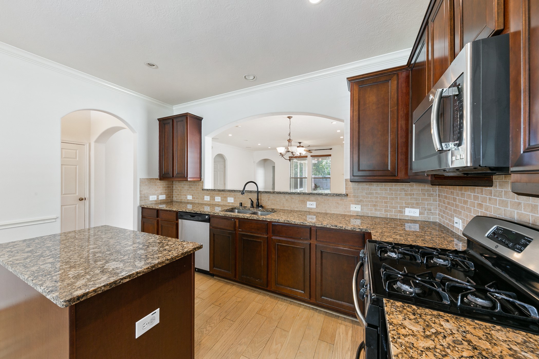 24527 Spring Harbor Drive Spring, TX 77373 - Photo 5 of 22 This kitchen features dark wood cabinets, granite countertops, and stainless steel appliances. It has a spacious layout with an island and an open view into the adjoining living area, highlighted by arched doorways and a tiled backsplash.