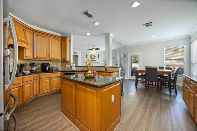 a kitchen with stainless steel appliances granite countertop wooden cabinets a refrigerator a stove a sink and dishwasher with wooden floor