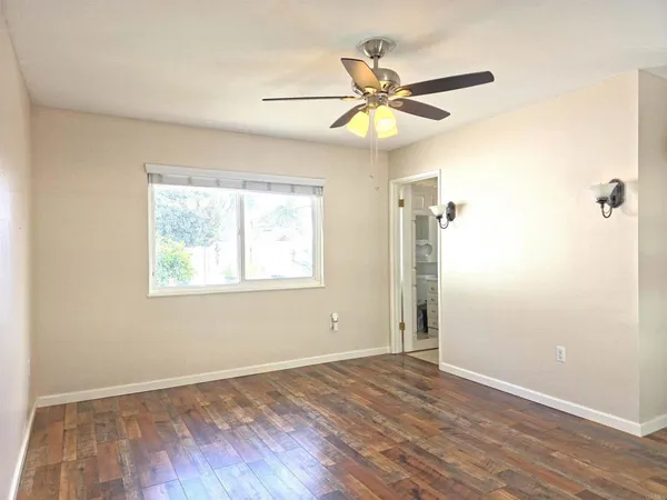 an empty room with wooden floor fan and windows