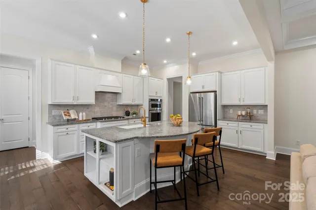a kitchen with stainless steel appliances kitchen island granite countertop a stove a sink a refrigerator and white cabinets with wooden floor