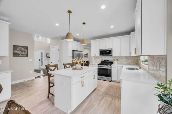 a large white kitchen with stainless steel appliances granite countertop a stove a sink a refrigerator and a dining table with wooden floor