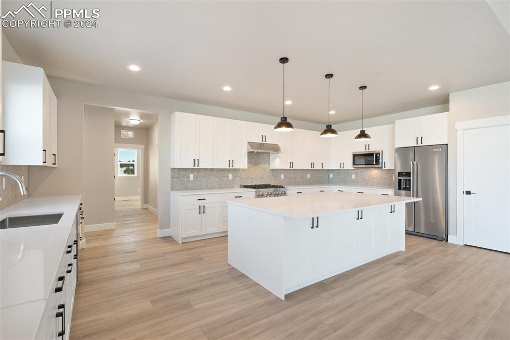 17615 Blacksmith Drive Peyton, CO 80831 - Photo 12 of 41 a large white kitchen with kitchen island a sink a stove a refrigerator and white cabinets with wooden floor