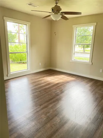 an empty room with wooden floor chandelier fan and windows