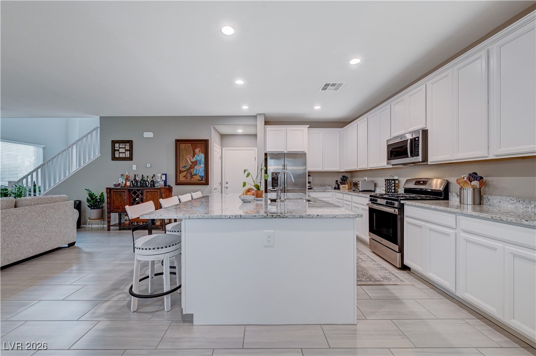 3826 Asia Road North Las Vegas, NV 89032 - Photo 11 of 30 Kitchen with stainless steel appliances, white cabinets, a kitchen breakfast bar, a center island with sink, and light stone counters