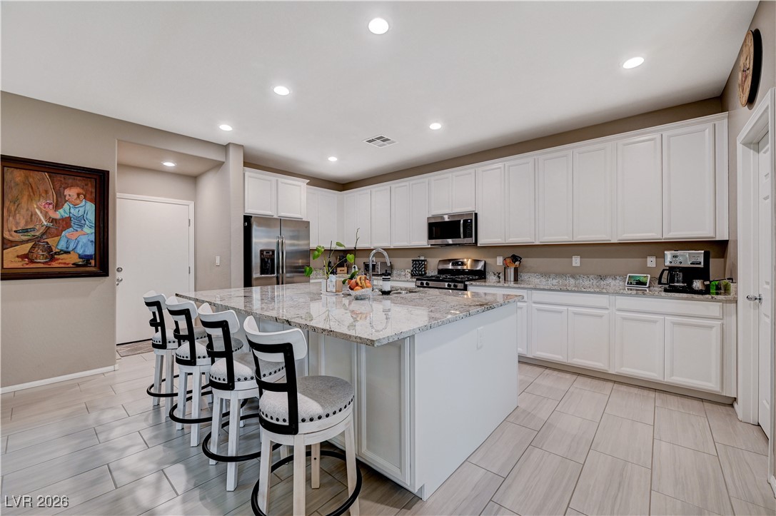 3826 Asia Road North Las Vegas, NV 89032 - Photo 10 of 30 Kitchen with white cabinets, light stone counters, appliances with stainless steel finishes, recessed lighting, and a kitchen breakfast bar
