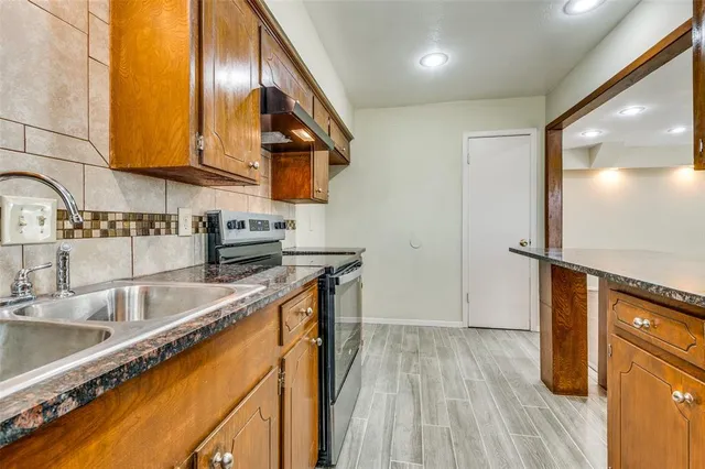 a kitchen with stainless steel appliances granite countertop a sink a stove and a wooden floors