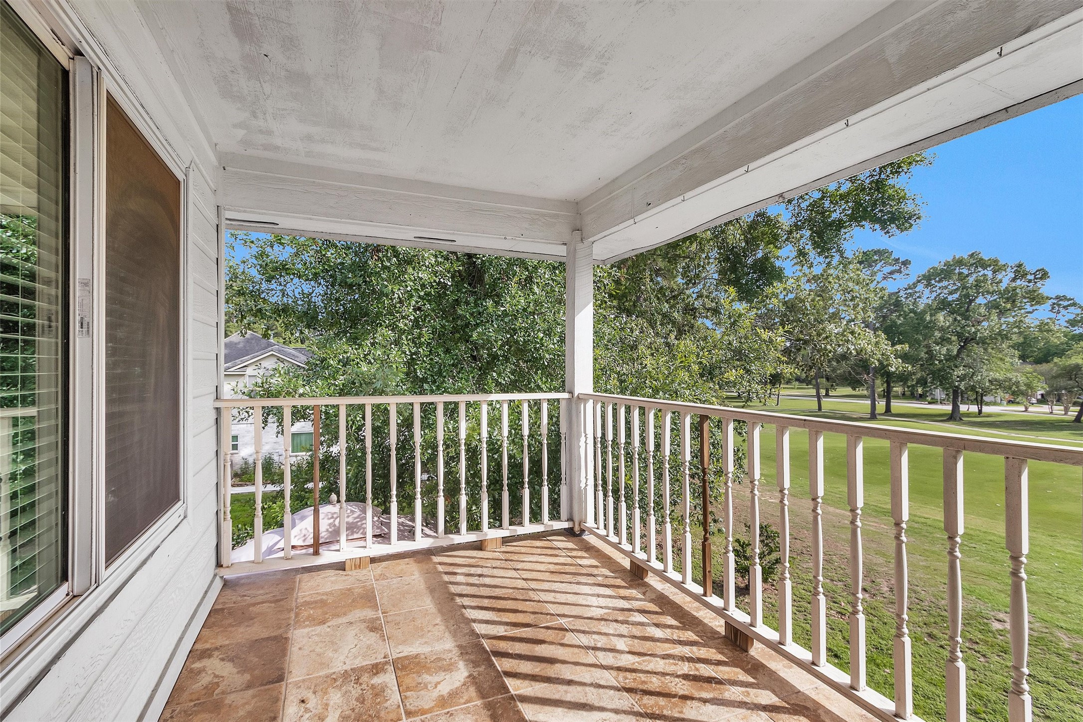 23 Alba Road Montgomery, TX 77356 - Photo 31 of 37 This photo showcases a charming, covered balcony with tiled flooring and white railings, offering a serene view of a lush, tree-lined landscape. Ideal for relaxation.